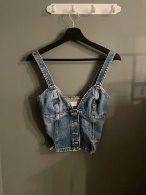 Blå denim korsettopp med knappar - Trendig blå denim korsettopp med breda axelband och knappar framtill. Toppen har en croppad passform och markerade sömmar för en snygg siluett. Perfekt att styla med höga jeans eller kjol för en cool look. Tryck köp nu❤️