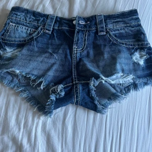 Blå jeansshorts med fransig kant - Snygga blå jeansshorts från Gina 14+ med fransig kant och slitna detaljer framtill. Klassisk femficksmodell med vita kontrastsömmar och coola bakfickor med dekorsömmar. Perfekta för sommarens alla häng och festivaler eller under kallare tider med ett par strumpbyxor🥰 Säljer då de inte passar och råka riva av lappen så kunde inte lämna tillbaka, aldrig använda.❤️