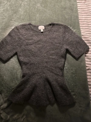 Grå stickad topp från H&M - Mysig trendig grå stickad topp från H&M med korta ärmar och utsvängd peplum-nederdel och volang vid nederdelen. Perfekt för dig som gillar en feminin siluett och vill ha något bekvämt men ändå stilrent. Enkel att matcha med både jeans och kjol.❣️❣️❣️❣️