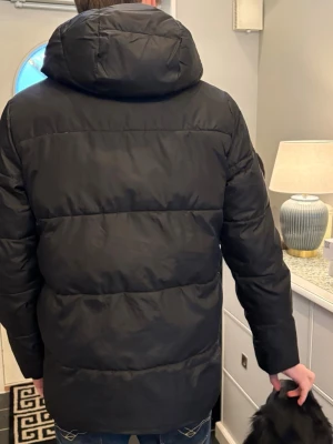 Svart pufferjacka från Calvin Klein - Säljer en svart pufferjacka från Calvin Klein Jeans med huva och quiltad design. Jackan har en diskret logga på bröstet och dragkedja framtill. Perfekt för kalla dagar och riktigt snygg till jeans eller hoodie.