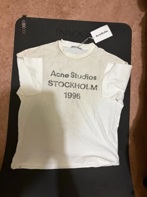 Vit Acne Studios t-shirt XS - Vit t-shirt från Acne Studios med tryck 'Acne Studios STOCKHOLM 1996' på bröstet. Klassisk rund hals och korta ärmar. Tillverkad i mjuk bomull, perfekt för en clean och enkel look.