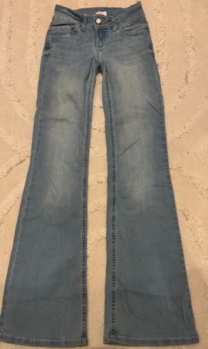 Lågmidjade Bootcut jeans  från Nelly - Snygga lågmidjade bootcut jeans från Nelly i ljusblå denim med dubbla knappar framtill. Jeansen har coola rosa detaljer på bakfickorna. Perfekt passform och mjukt material som sitter skönt.