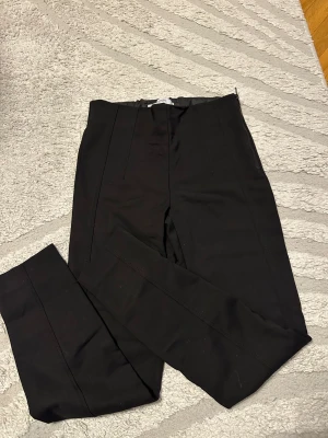 Svarta kostymbyxor från Mango - Snygga svarta kostymbyxor från Mango med hög midja och raka ben. Byxorna har pressveck framtill och en diskret dragkedja i sidan för en clean look. Materialet är mjukt och har en lätt stretch som gör dem bekväma att bära hela dagen.