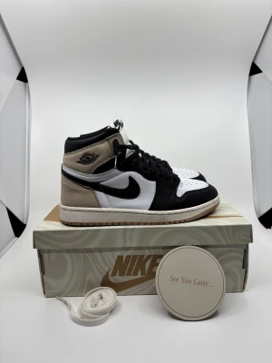 Nike Air Jordan 1 Latte Highs - Nike Air Jordan 1 Latte med högt skaft, svart swoosh och snörning. Allt extra som snören och sånt ingår. Pris 600kr, kan gå ned vid snabb affär. Storlek 39. Liten svart fläck på mockan, går säkert bort. Materialet är en mix av skinn och mocka, vilket ger en lyxig känsla. Perfekt för dig som vill sticka ut med klassiska sneakers.