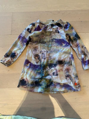 Hundmönstrad klänning från Molo - Superfin klänning från Molo med unikt hundmönster i lila, beige och gröna toner. Långärmad modell med rund hals och lätt utställd kjol. Mjuk och stretchig bomull som är skön att ha på sig. Perfekt för dig som älskar djur och vill sticka ut!