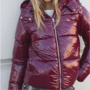 Vinröd pufferjacka från Nelly - Säljer en vinröd pufferjacka med glansig finish och huva. Jackan har dragkedja framtill, två sidofickor och quiltad design. Perfekt för kalla dagar och har en cool, oversized look som är enkel att styla med jeans eller sneakers. Knappt använd💞