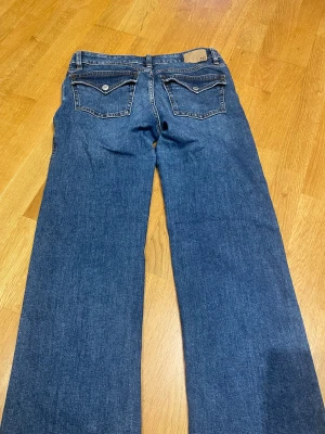 Blå bootcut jeans från lager 157 - Snygga blå jeans från 157 med bootcut passform och klassiska fem fickor. Jeansen har kontrastsömmar, knapp och dragkedja framtill samt coola fickdetaljer bak. Modellen heter '90's Boot' och är tillverkad i slitstarkt denimtyg. Den är i storlek M short