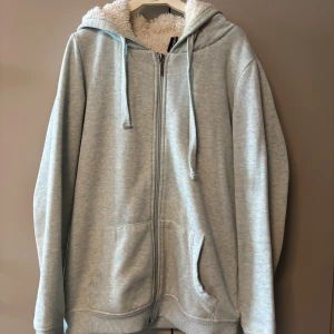 Ljusblå hoodie med fluffig fleece - Mysig ljusblå hoodie från FB Sister i storlek XS. Utsidan är mjuk bomullsmix och insidan har fluffigt vitt fleecefoder. Tröjan har huva med snörning, dragkedja framtill och två stora fickor. Perfekt för chill dagar och när du vill vara extra bekväm. Använd en del men fortfarande som om den är ny på insidan.