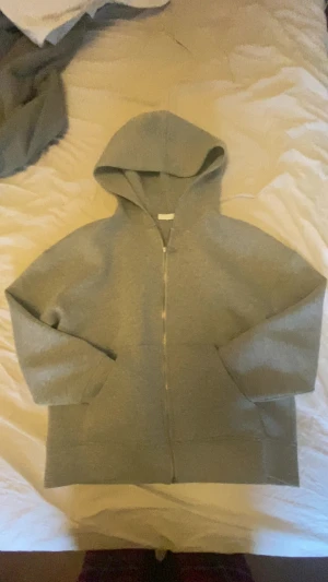 Grå hoodie med dragkedja och huva - Säljer en enkel grå hoodie med dragkedja och huva. Tröjan har långärmade ärmar och en loose passform, perfekt för chill dagar. Materialet känns som mjuk bomull eller polyester. Snygg att slänga på sig när det är lite kyligt ute.  OBS!! Storleks lappen finns inte men tröjan ska vara m men passar s