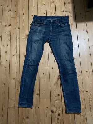 Levi's 512 blå jeans W32 L34 - Snygga Levi's 512 jeans i klassisk blå tvätt med smal passform och raka ben. Jeansen har fem fickor, knapp och dragkedja fram samt det ikoniska läderpatchen bak i midjan. Perfekta för dig som gillar en modern och stilren look.
