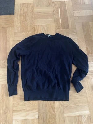 Blå merinoulltröja från Uniqlo XS - Mjuk och stilren mörkblå merinoulltröja från Uniqlo i storlek XS. Tröjan har rund hals, långa ärmar och ribbade muddar vid ärmslut och nederkant. Perfekt för dig som gillar klassisk och enkel stil med lyxig känsla.