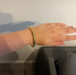 Guldfärgat armband i rund form - Snyggt armband i guldfärg med rund, chunky design och diskret räfflad yta. Perfekt accessoar för att lyfta din outfit med en stilren och modern touch. Armbandet är stelt och har en minimalistisk look som passar till många stilar.