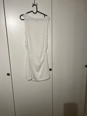 Vit ärmlös kortklänning H&M Divided - Säljer en vit, ärmlös kortklänning från H&M Divided i storlek L. Klänningen har en tight passform och snygg rynkdetalj på sidan som ger en cool look. Tillverkad i mjukt och stretchigt material, perfekt för varma dagar.