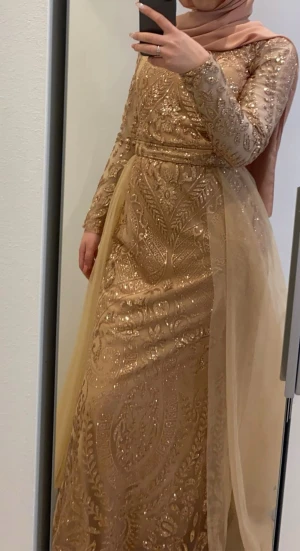 Glittrig champagnefärgad långklänning - Säljer en magisk långklänning i champagnefärg med glittriga detaljer. Klänningen har lång ärm, markerad midja och släp av tyll som ger extra volym. Perfekt för dig som vill sticka ut med elegans och glamour. Storlek passar både XS/S. Köpt i Turkiet och använd bara en gång. Pris kan diskuteras vid snabb affär