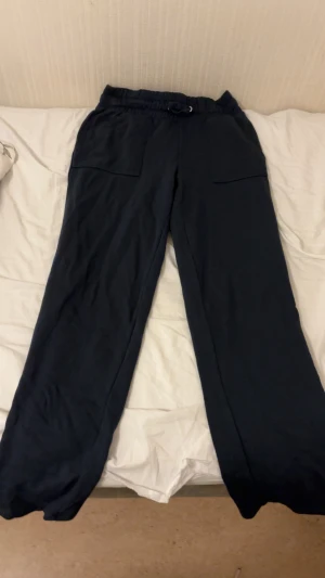 Mörkblå mjukisbyxor från 157, storlek M - Snygga mörkblå mjukisbyxor från 157 med bred resår i midjan och två stora fickor framtill. Byxorna har en loose passform och är gjorda i mjukt bomullsmaterial, perfekta för chill dagar. Passar dig som gillar bekväma och stilrena plagg.