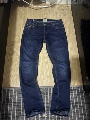 Morris Steve Satin Jeans blå 34/32 - Snygga mörkblå jeans från Morris med kontrasterande gul söm och coola broderade detaljer på fickorna. Modellen är straight fit med klassisk femficksdesign och läderpatch bak. Perfekt för dig som gillar stilrena och tidlösa jeans. Priset kan alltid diskuteras!!