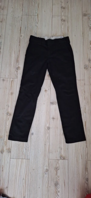 Svarta slim fit byxor från Dickies - Svarta byxor från Dickies i slim fit-modell med raka ben och klassisk look. Byxorna har bälteshällor, två bakfickor och diskret Dickies-logga ovanför ena bakfickan. Perfekta för dig som gillar stilrena och enkla byxor.
