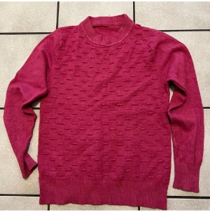 Mörkrosa stickad tröja med struktur - Snygg mörkrosa stickad tröja med rund hals och långärmade. Framsidan har ett coolt upphöjt strukturmönster som ger extra vibe. Ribbad kant vid hals, ärmslut och nederkant. Perfekt för dig som gillar färg och vill ha något unikt i garderoben.
