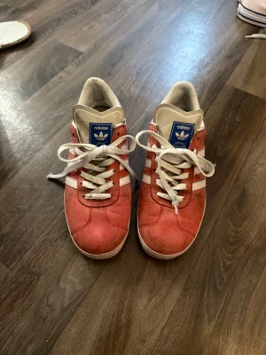 Adidas Gazelle röd mocka sneaker Str 38.5 - Säljer ett par Adidas Gazelle sneakers i röd mocka med vita detaljer💕Skorna har snörning, platt sula och rund tå. Adidas-logga i blått på hälen och tungan. Ganska använda men super fina fotfarande🤗