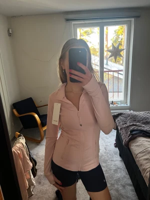 Ljusrosa zip-hoodie från Lululemon, strawberry milkshake - Supersnygg ljusrosa hoodie från Lululemon med dragkedja framtill och två fickor. Slimmad passform och långa ärmar.  Perfekt för träning eller chill.