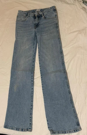 Blå bootcut jeans från Lager 157 - Snygga ljusblå jeans från Lager 157 med klassisk femficksdesign och en bakficka med lock och knapp. Modellen har bootcut-ben och normal passform, perfekt för dig som gillar retrovibbar. Jeansen är tillverkade i jeansmaterial och har en rak låg midja.
