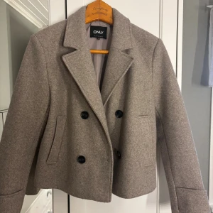 höstig kappa - Jättefin, kort, beige/grå kappa från Only. Ganska mycket använd men väldigt bra skick ändå. Säljer då den inte kommer till användning. Pris kan diskuteras