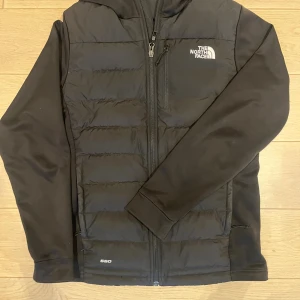 Svart dunjacka från The North Face - Säljer en svart dunjacka från The North Face med huva och dragkedja framtill. Jackan har quiltad framsida, sidofickor med dragkedja och diskret logga på bröstet. Perfekt för kyliga dagar och enkel att matcha med allt. 550 fill power.