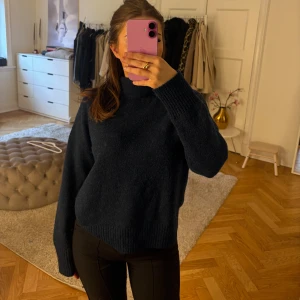 Mörkblå stickad polotröja - Mysig mörkblå stickad polotröja med hög hals och långa ärmar. Tröjan har en loose passform och ribbade muddar vid ärmslut och nederkant. Perfekt för kyliga dagar och enkel att styla