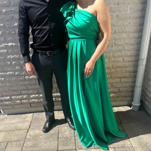 Grön långklänning med oneshoulder - Säljer en elegant grön långklänning med oneshoulder och volangdetalj vid axeln. Klänningen har ett svepande fall och markerad midja, perfekt för dig som vill sticka ut med en färgstark look. Materialet är i satin  och känns lyxigt mot huden. Går att sy in eller sy ut samt korta ner.  Inköps pris 5000 säljer 3000 finns i Göteborg och Jönköping. 