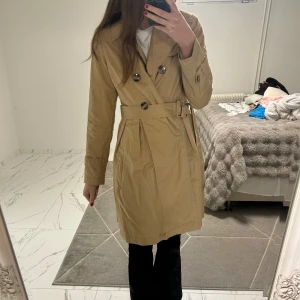 Beige trenchcoat från Lindex, strl 38 - Snygg beige trenchcoat från Lindex i klassisk modell med dubbelknäppning, bälte i midjan och långa ärmar. Jackan har stilrena detaljer och är perfekt för dig som gillar en clean och tidlös look. Brukar ha storlek 36 men passar även mig perfekt ❤️