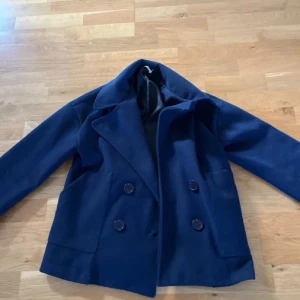 Mörkblå skepparkavaj XS/S från Ivyrevel - Säljer en mörkblå kappa från design by si, l i storlek XS/S. Jackan har dubbelknäppning med stora knappar, bred krage och är tillverkad i ullblandning med foder i polyester. Perfekt för dig som gillar klassisk stil med modern twist.