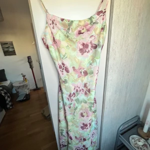 Blommig långklänning från Gina Tricot - Supersöt långklänning från Gina Tricot med blommigt mönster i pastelliga toner av rosa, grön och beige. Klänningen har smala axelband och en mjukt draperad halsringning. Perfekt för sommarens alla tillfällen! Använd bara en gång!