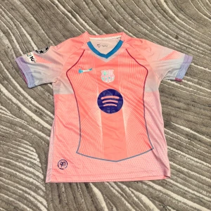 Barcelona Lamine Yamal #10 fotbollströja - Snygg Barcelona fotbollströja med Lamine Yamal och nummer 10 på ryggen. Tröjan är kortärmad och har en unik design i ljusrosa och lila toner med blå detaljer. Tillverkad i Nike Dri-FIT material som andas. Champions League-märke på ärmen och Spotify-logga på bröstet.