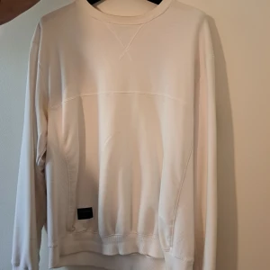 Vit sweatshirt från Marshall Artist 2XL - Vit långärmad sweatshirt från Marshall Artist i storlek 2XL. Tröjan har rund hals, ribbade muddar och svarta patchdetaljer på sidan och ärmen med logotyp. Mjuk bomullskvalitet och clean design.