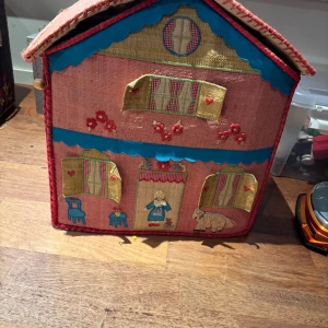 Rice förvaringshus i rotting - Charmigt handgjort förvaringshus från Rice i rotting med broderade detaljer. Perfekt för leksaker eller förvaring i barnrummet. Fint skick, mindre slitage på hörn och kanter.  design med fönster, dörrar och figurer. Praktiskt lock och handtag för enkel förflyttning.