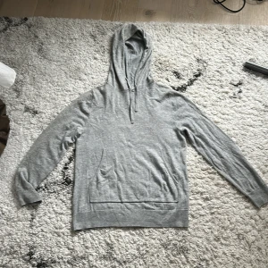 Grå hoodie från Filippa K i bomull - Säljer en stilren grå hoodie från Filippa K i mjuk bomull. Tröjan har huva med snörning, känguruficka och långärmad passform. Perfekt för en chill och avslappnad look.