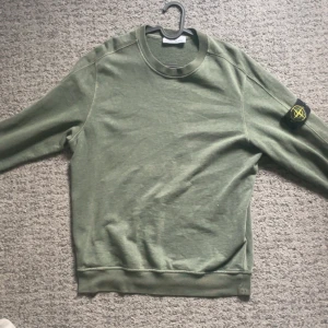 Grön Stone Island sweatshirt - Säljer en grön sweatshirt från Stone Island med klassisk patch på ärmen. Tröjan har rund halsringning, långa ärmar och är tillverkad i mjuk bomull. Perfekt för dig som gillar streetwear och vill ha en clean look.
