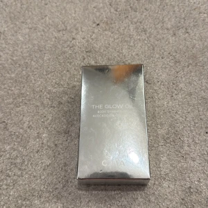 CAIA The Glow Oil Body Shimmer - The Glow Oil från CAIA är en lyxig body shimmer-olja med avokadoolja och vitamin E. Kommer i en snygg fyrkantig glasflaska med silvrig kork och skimrande guldig olja som ger glow till huden. Förpackningen är metallic-silver och känns riktigt exklusiv. " denna är aldrig använd!"