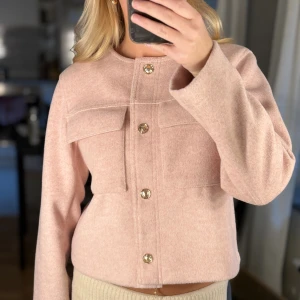 Ljusrosa ulljacka från Zara - Passar perfekt till hösten 🍁Supersnygg ljusrosa jacka från Zara i ullmix med raka linjer och guldiga knappar framtill. Jackan har två stora bröstfickor och lång ärm, perfekt för dig som gillar stilren och trendig look. 