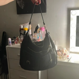 Svart axelväska med gulddetaljer - Säljer en jättefin nästan oanvänd väska med guldiga och coola detaljer! Den rymmer mycket och har många fickor så den är väldigt praktisk för skolan. Skriv vid frågor💕