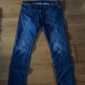 Jack&jones Jeans - Säljer ett par blå slim fit jeans från Jack & Jones, modell Glenn. Klassisk femficksdesign med snygga kontrastsömmar och normal midja. Jeansen är gjorda i denim och har en smal passform som sitter snyggt längs benen. Perfekta för dig som gillar stilrena och bekväma jeans.