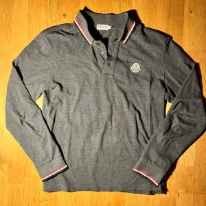 Moncler Pike - Stilren och riktigt fet långärmad piké från Moncler. Mörkgrå färg🤩. Hör av dig om du har några funderingar!