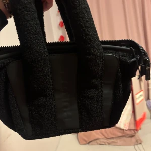 Svart handväska från Hunter - Helt ny handväska  med prislapp   från Hunter med grov textur och detaljer i syntetmaterial. Väskan har två breda handtag och dragkedja upptill. Perfekt för dig som vill ha en unik accessoar med stilren vibe. Ordinarie pris 3000 :- säljer den för 1000 kan gå ner vid snabba affär 