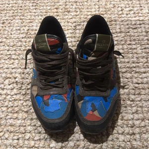 Valentino Garavani Rockrunner sneakers - Säljer ett par Valentino Garavani Rockrunner sneakers med unik camouflage-mönstrad ovandel i blått, rött, beige och svart. Skorna har bruna mockadetaljer, svarta snören och robust gummisula. Perfekt för dig som vill sticka ut med exklusiva och färgstarka sneakers. Ingen box eller så, hör av er vid funderingar.