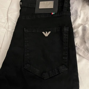 Svarta jeans från Emporio Armani - Svarta jeans från Emporio Armani med klassisk femficksdesign och silverfärgad logga på bakfickan. Jeansen har raka ben och är tillverkade i ett mjukt bomullsmaterial med en stilren look. Perfekta för dig som gillar minimalistisk och snygg stil.