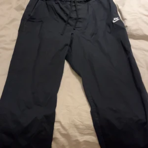 Svarta mjukisbyxor från Nike XXL - Svarta mjukisbyxor från Nike i storlek XXL. Byxorna har resår och snörning i midjan samt klassisk Nike-logga på ena benet. Perfekta för chill eller träning, med en loose fit och bekvämt material.
