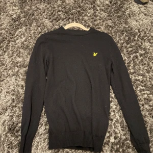 Mörkblå stickad tröja från Lyle & Scott - Mörkblå stickad tröja från Lyle & Scott med klassisk gul logga på bröstet. Tröjan har rund halsringning, ribbade muddar och är långärmad. Perfekt för dig som gillar stilrena plagg. Köpte den för 800 kr på mq och den är i väldigt bra skick