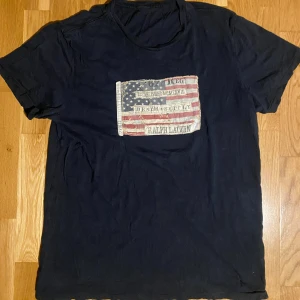 Ralph Lauren USA t-shirt - En snygg och eftertraktad t-shirt. Den har flera hål och etikett saknas. Vill gissa på att den är i storlek M/L passar båda bra. Ifall mer frågor eller nogare bilder på slitage så skriv gärna!