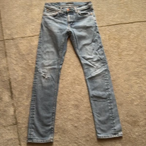 Ljusblå Lean Dean jeans från Nudie - Ljusblå skinny jeans från Nudie med klassiska femficksdetaljer, slitning och hål på vänster knä samt Nudie-logga på bakfickan. Jeansen har smal passform och är tillverkade i mjukt denimtyg med snygga kontrastsömmar.