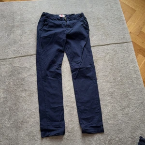 Mörkblå chinos från American Outfitters - Snygga mörkblå chinos från American Outfitters med klassisk passform. Byxorna har dragkedja, knappstängning och bälteshällor. Perfekta för en clean och stilren look. Tillverkade i mjuk bomull för skön känsla hela dagen.